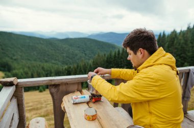 Turist bir dağ evinin terasında bir masada oturur ve yürüyüş sırasında ocakta yemek hazırlar..