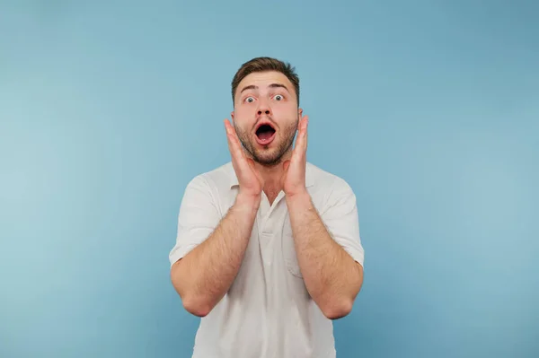 stock image Shocked bearded man in white t-shirt looking at camera with surprised face isolated on blue background