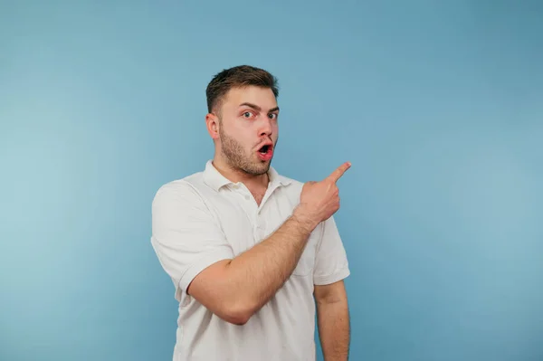 Shocked Young Man White Shirt Stands Blue Background Points His — стоковое фото