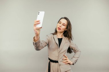 Beautiful business woman in a suit taking a selfie on a beige background and taking a selfie with a serious face.
