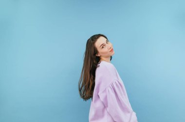 Mor kazaklı tatlı esmer kadın mavi arka planda duruyor ve ciddi bir yüzle kameraya bakıyor..