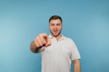 Yüzünde gülümseme olan neşeli bir adam mavi bir arka planda duruyor ve yüzünde bir gülümsemeyle kameraya bakıyor..