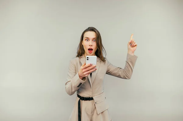 Shocked Woman Suit Stands Beige Background Smartphone His Hands Shows — Zdjęcie stockowe