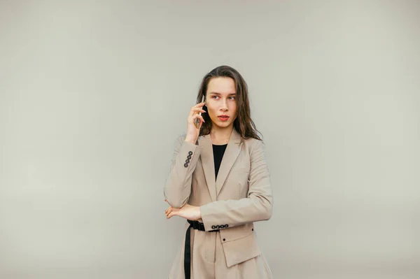 Beautiful Woman Jacket Stands Beige Background Talks Phone Serious Face — Stok fotoğraf