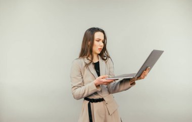 Elinde dizüstü bilgisayarı olan ceketli güzel bir kadın bej arka planda duruyor ve çalışıyor. Dikey.