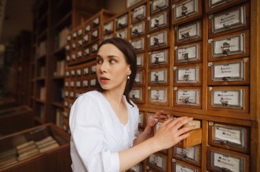 Kütüphane arşivlerinde bilgi arayan güzel bir kadın, ciddi bir yüz ifadesiyle başka yere bakıyor..
