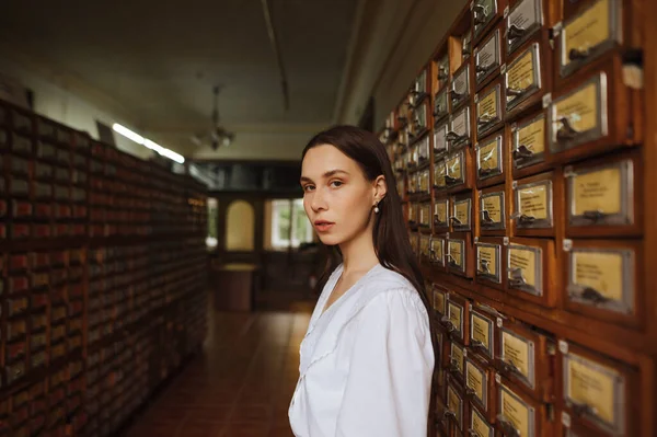 Beyaz bluzlu güzel bir kadının portresi kütüphane arşivlerinde duruyor ve ciddi bir yüzle kameraya poz veriyor..
