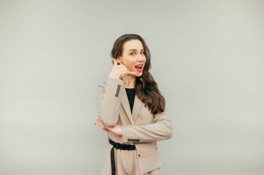 Takım elbiseli çekici bir bayan çağrı jesti gösteriyor ve yüzünde bej bir arka planda izole edilmiş bir gülümsemeyle kameraya bakıyor. Kadın bir hareket gösterirse beni ara.