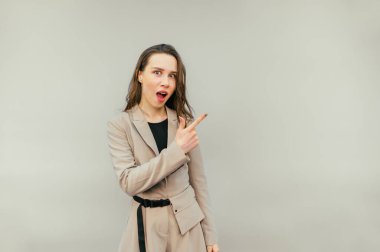 Bej arka planda ceketli, şaşırmış bir kadının portresi. Şok olmuş bir yüzle kameraya bakıyor ve fotokopi çekerken parmağını gösteriyor.