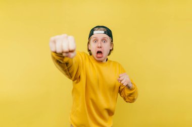 Funny guy with a scared face shows a fist to the camera on a yellow background.