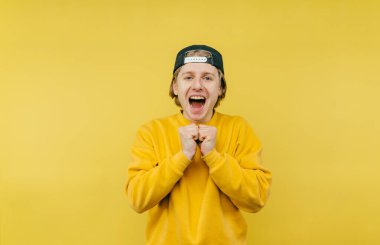 Sarı arka planda svetşörtlü ve şapkalı neşeli çocuk portresi, kameraya bakıyor ve mutlu..