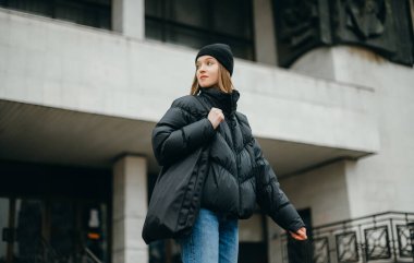 Kışlık ceketli ve şapkalı şık bir kadın elinde alışveriş çantasıyla caddede yürüyor..