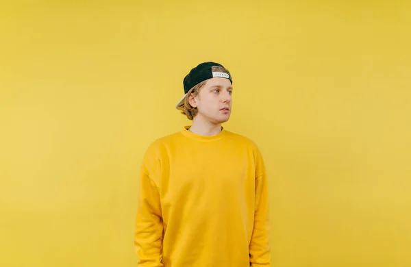 Handsome man in cap and yellow sweatshirt isolated on yellow background and looks away with a serious face.