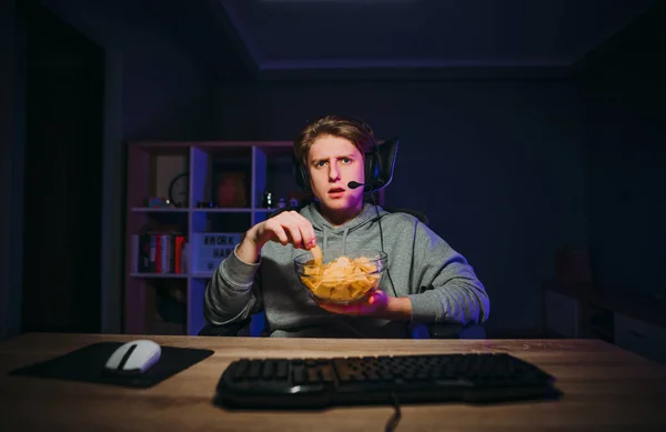 Serious Young Man Headset Sits Night Computer Eats Chips Plate — Stockfoto