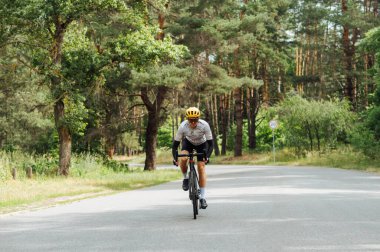 Spor ekipmanlı genç adam şehrin dışındaki ormanda trenlere biniyor ve asfalt bir yolda ilerliyor..