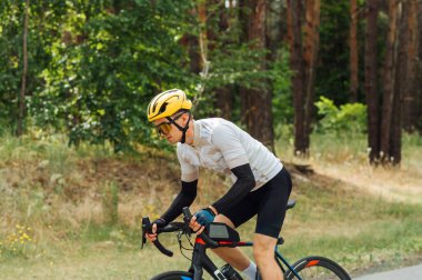 Profesyonel bisikletçi şehir dışında ormanda bisiklet sürüyor, ciddi yüzlü bir bisiklet sürüyor..