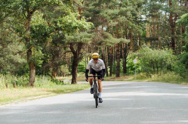 Spor ekipmanlı genç adam şehrin dışındaki ormanda trenlere biniyor ve asfalt bir yolda ilerliyor..