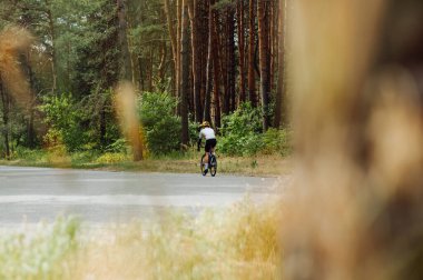 Spor giyimli erkek bisikletçi şehrin dışındaki ormanda asfalt bir yolda..