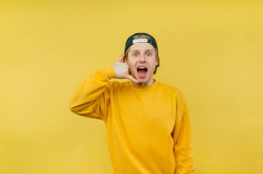 Şapkalı ve günlük kıyafetli neşeli bir adam parmaklarıyla yüzük jesti yapıyor ve duygusal bir yüzle kameraya bakıyor..