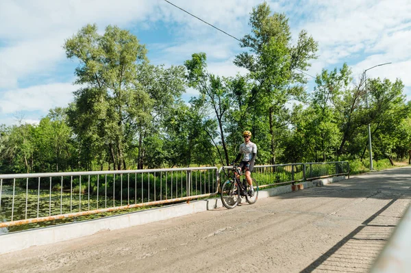 年轻的运动员骑着自行车站在公园的桥上休息 — 图库照片