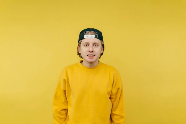 Cute guy in a cap and casual clothes isolated on a yellow background, looking at the camera and smiling.