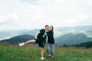 Positive young tourist couple having fun in the mountains hugging and posing for the camera with a smile on their face against a background of beautiful natural scenery