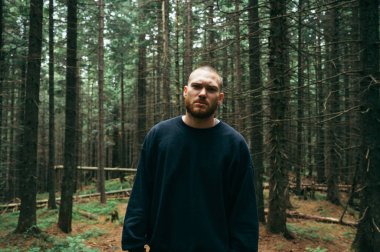 Portrait of a handsome bearded hiker in casual clothes in the forest while climbing the mountains, looking at the camera with a serious face.