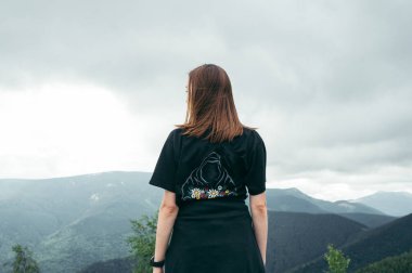 The back of a female tourist reached the top of the mountain, she stands and looks at the beautiful scenery.