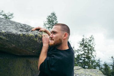 Handsome male rock climber climbing stones on a cliff, hanging in the air and looking away with a smile on his face.