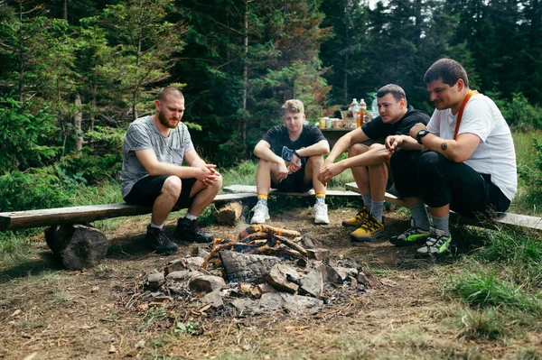 Group of male hikers sitting by campfire and camping in the mountains during a hike. Active recreation in the mountains.
