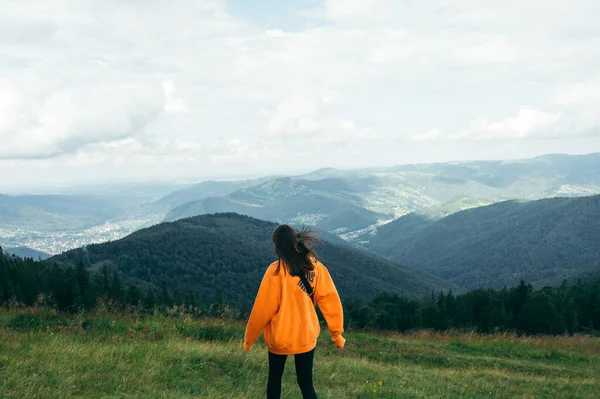 Photo Back Female Tourist Orange Sweatshirt Standing Mountains Meadow Looking — Stock Photo, Image
