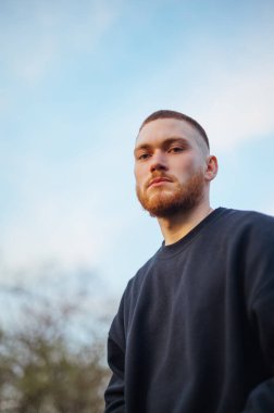 Portrait of a stylish young man with a red beard on the street, looking at the camera with a serious face, bottom view.