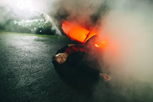Man Involved Car Accident Lying Ground Night Smoke Background Burning — Stock Photo, Image