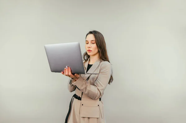 Concentrated attractive woman in suit working on laptop on beige wall background with serious face. Business woman with laptop isolated on a beige background.