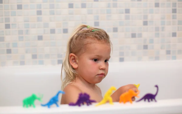 Liten flicka leker med leksak dinosaurier i badkaret — Stockfoto