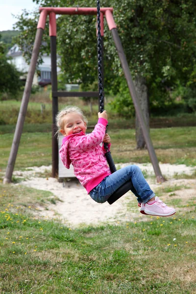 Happy toddler girl on a swing in city park — Stock Photo, Image