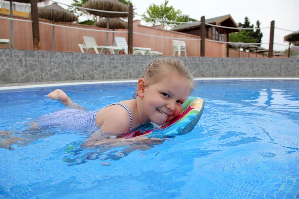 Niña divertida nada en una piscina con una pequeña tabla de bodyboard — Foto de Stock