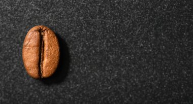 One coffee bean dark roasted espresso on a blured black background.