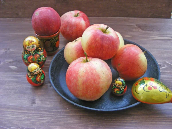 Samenstelling van de rode en gele appels op zwarte gietijzeren plaat met traditionele Russische nesting dolls matrioshka en geschilderde lepel op bruin houten tafel — Stockfoto