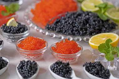 Bir sürü kırmızı ve siyah havyar. Cam kase ve elit somon havyarlı beyaz kaşıklar ve buzda tuzlu siyah Beluga mersin balığı yumurtası. Limonlu aperatifler, limonlu. Lezzetli aperatif. Şenlikli yemek. Lüks lezzetli yiyecekler.