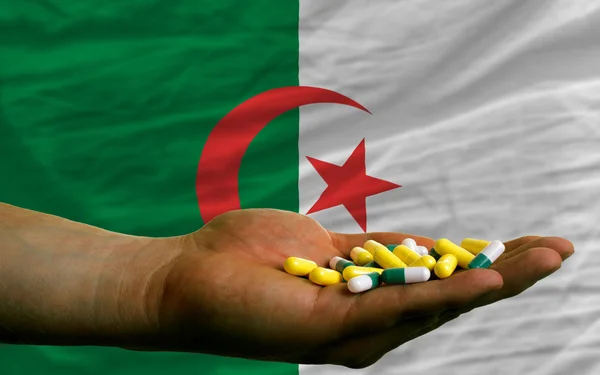 Holding pills in hand in front of algeria national flag — Stock Photo, Image