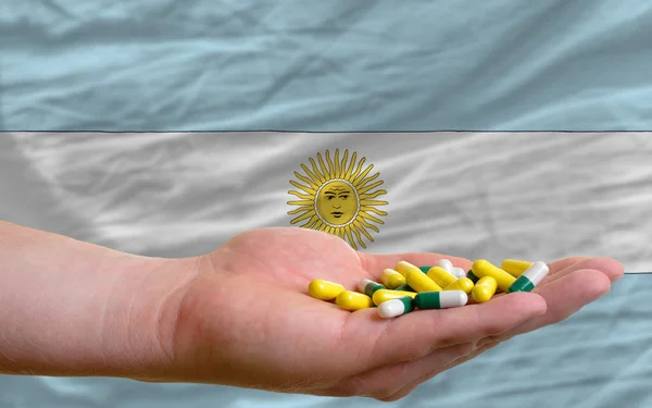 Holding pills in hand in front of argentina national flag — Stock Photo, Image