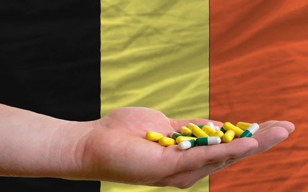 Holding pills in hand in front of belgium national flag — Stock Photo, Image