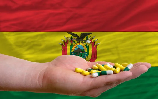 Holding pills in hand in front of bolivia national flag — Stock Photo, Image