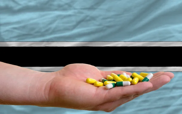 Holding pills in hand in front of botswana national flag — Stock Photo, Image