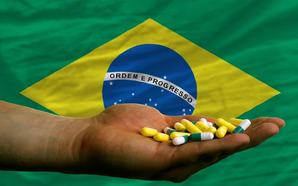 Holding pills in hand in front of brazil national flag — Stock Photo, Image