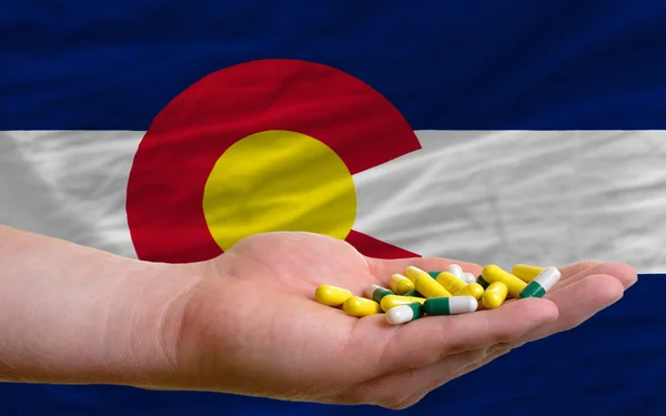 Sosteniendo píldoras en la mano frente a la bandera del estado de Colorado us — Foto de Stock