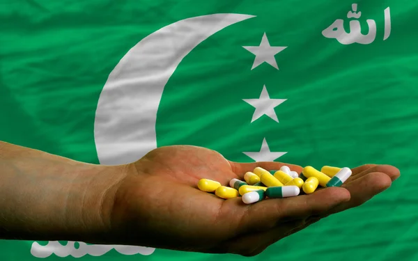 Holding pills in hand in front of comoros national flag — Stock Photo, Image