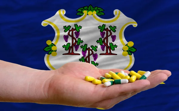 Segurando pílulas na mão na frente da bandeira do estado connecticut us — Fotografia de Stock