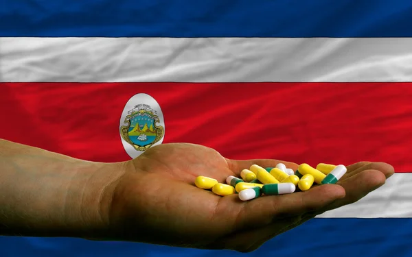 Holding pills in hand in front of costa rica national flag — Stock Photo, Image